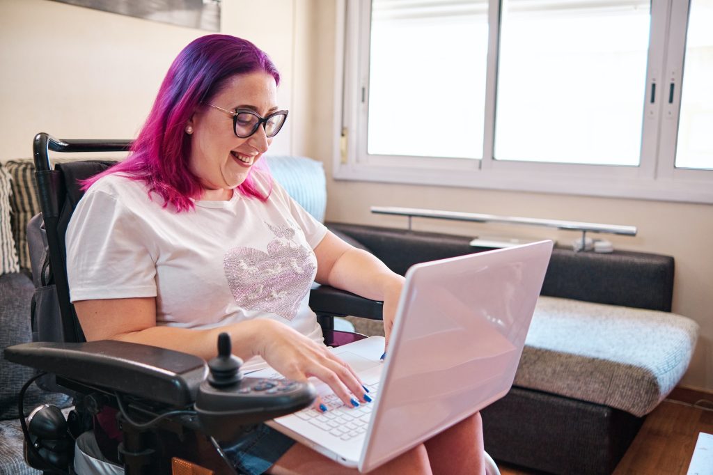 adult woman with disabilites in a wheelchair working at home with laptop